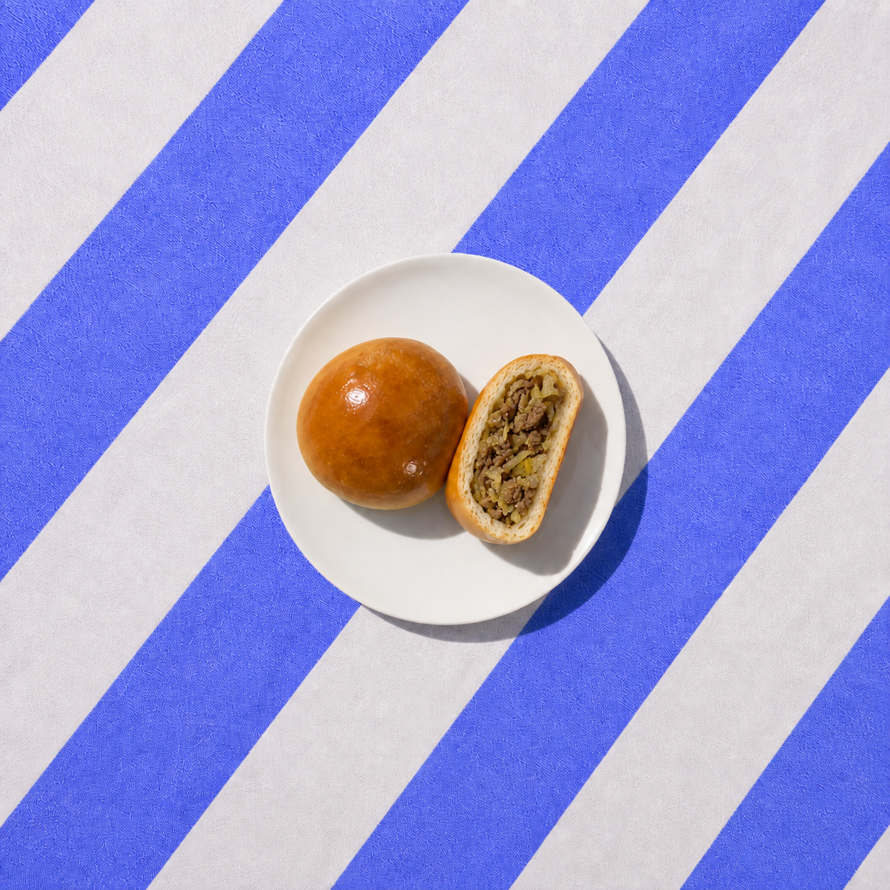 A beef bierock, one whole and one cut open, on a white plate over blue and white striped fabric