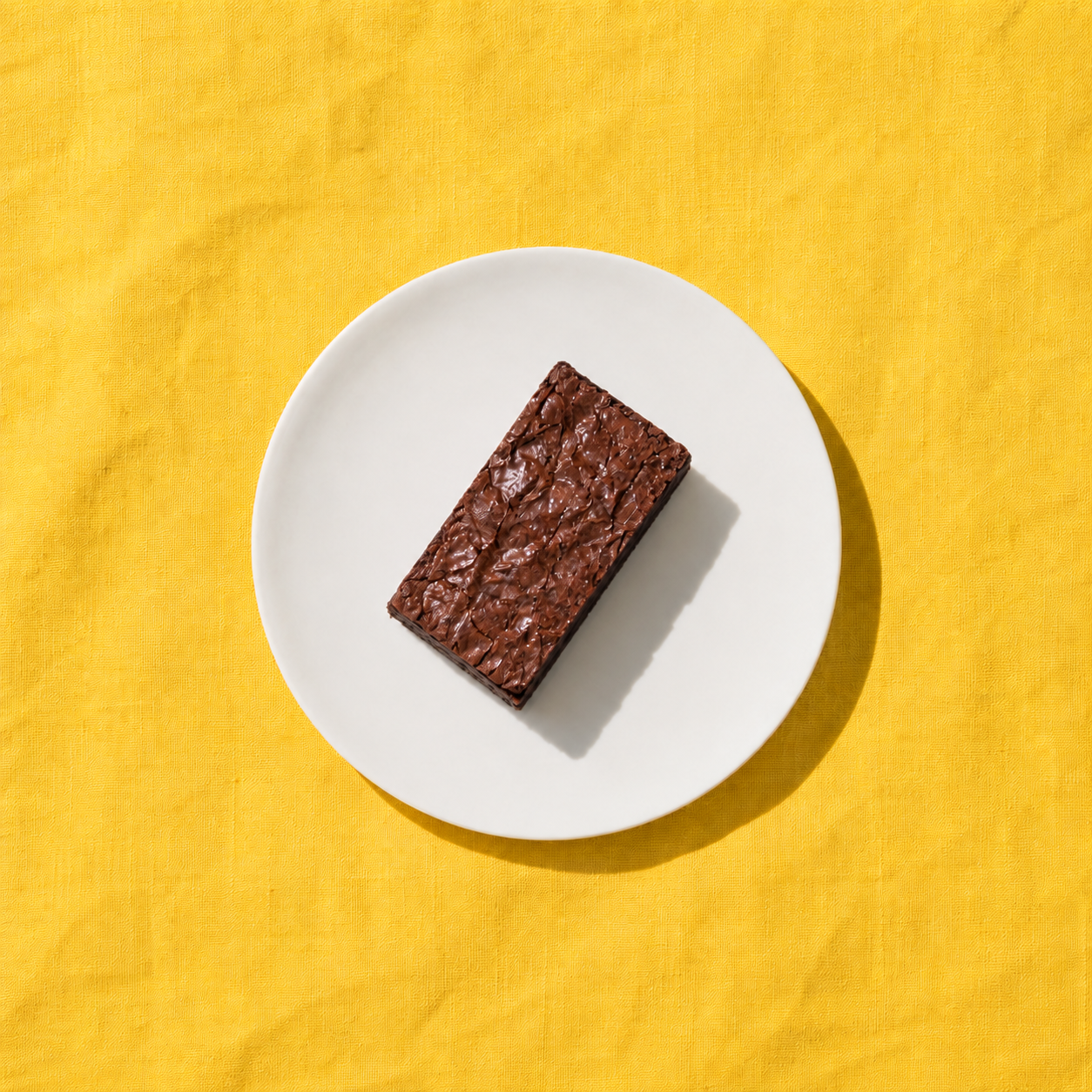 A chocolate brownie on a white plate over golden yellow fabric