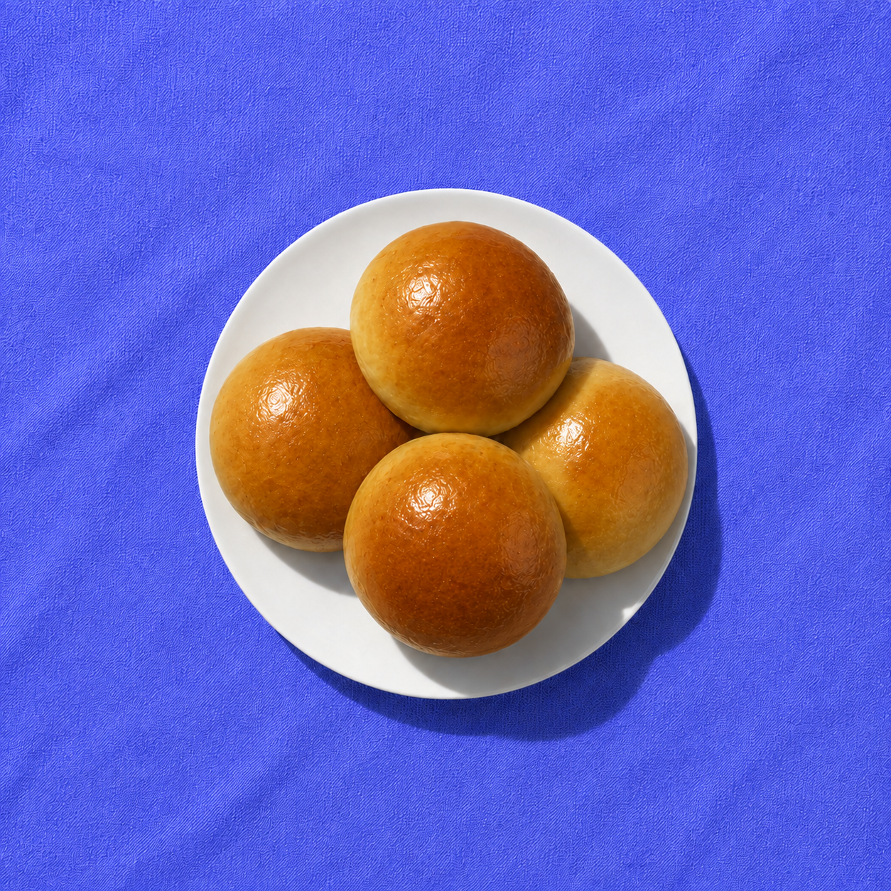 Four golden beef bierocks on a white plate over vivid blue fabric
